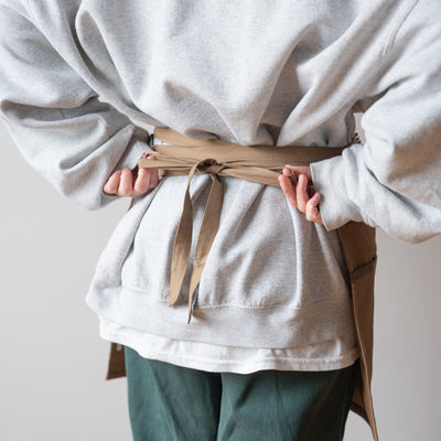 Tan utility apron worn by model, tied up in back